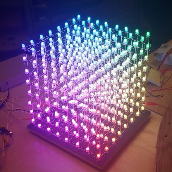 Several hundred glowing LEDs form a one foot tall cube on a table.